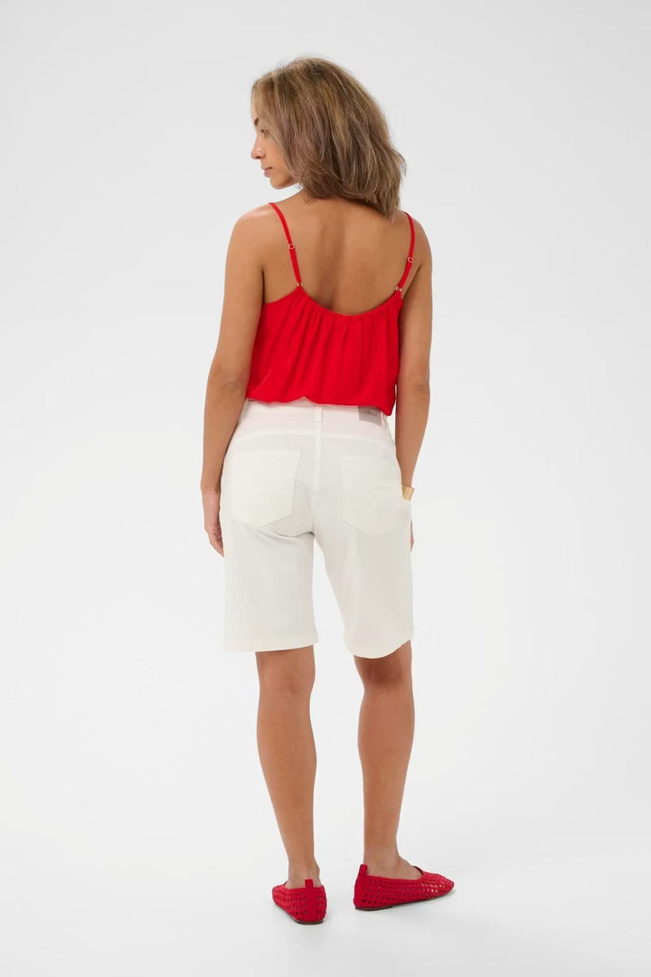 Femme portant un Bermuda classique coupe droite blanc, top rouge et mocassins, vue de dos, style estival moderne et polyvalent.