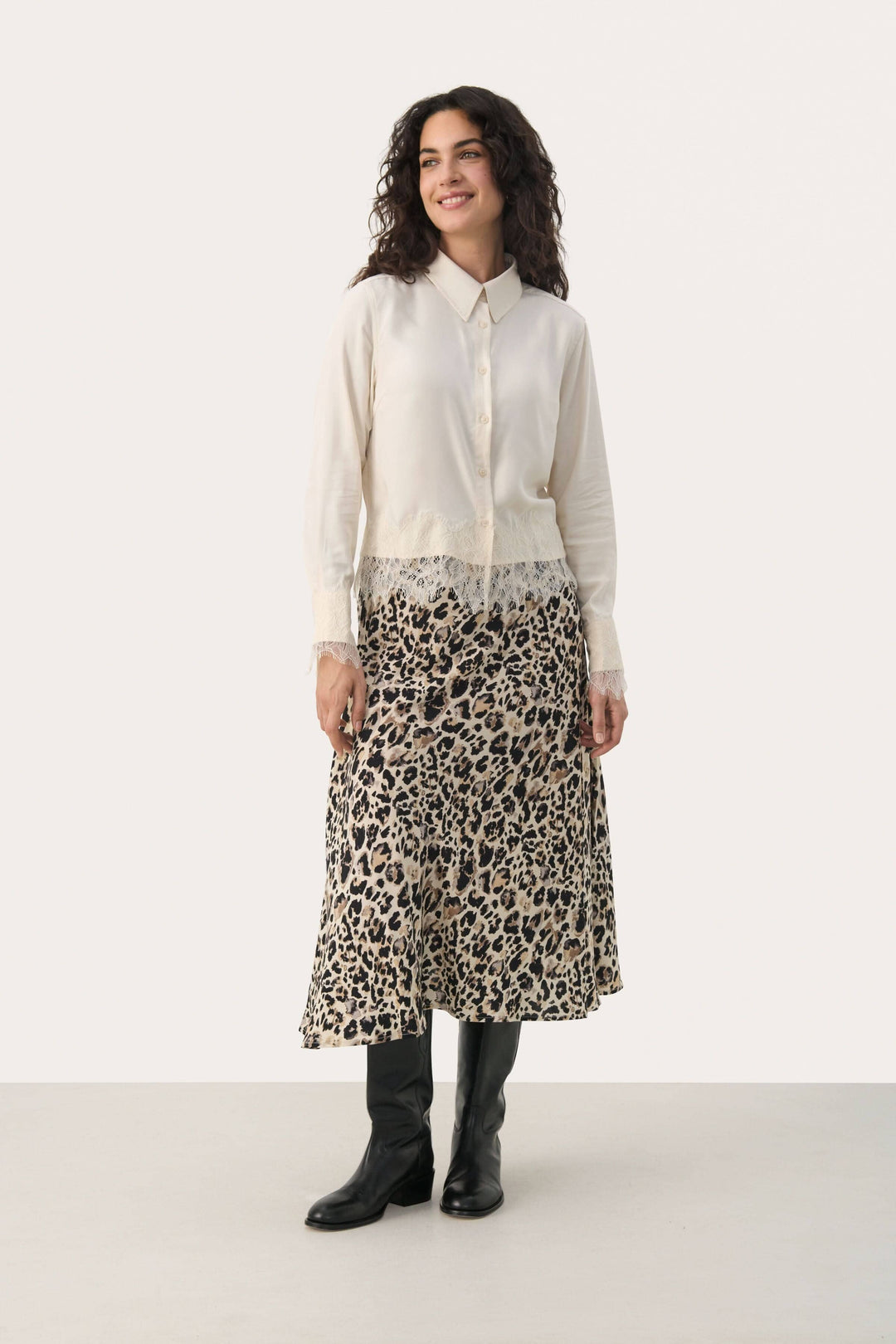 Femme portant une blouse Lenina élégante avec dentelle, associée à une jupe léopard longue et des bottes noires.