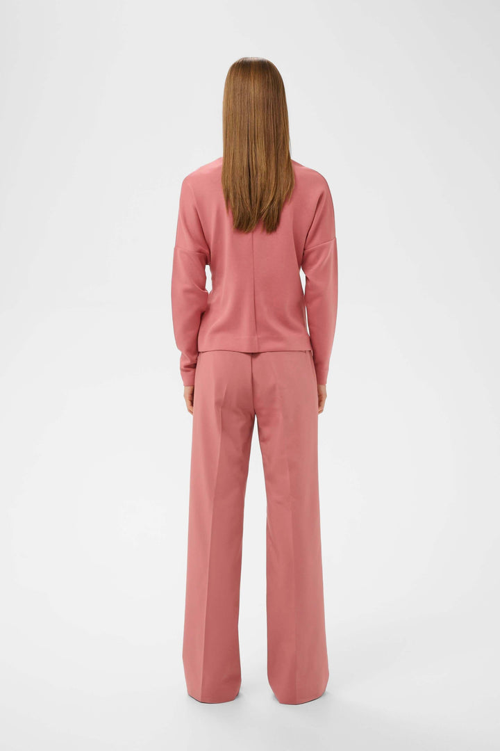 Person wearing a pink blouse and pants set, viewed from the back, showcasing a contemporary and flattering design with straight cut.