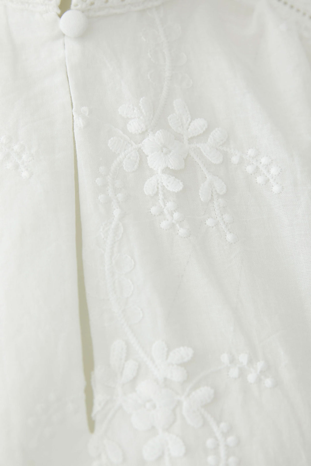 Blouse à broderies florales avec détail de broderie florale raffinée sur tissu blanc.