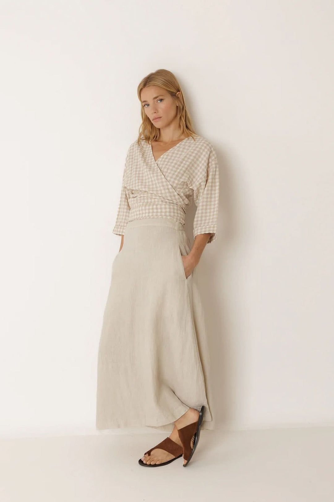 Femme portant une blouse cache-cœur à motif vichy avec manches 3/4, associée à une jupe longue beige, style contemporain et féminin.