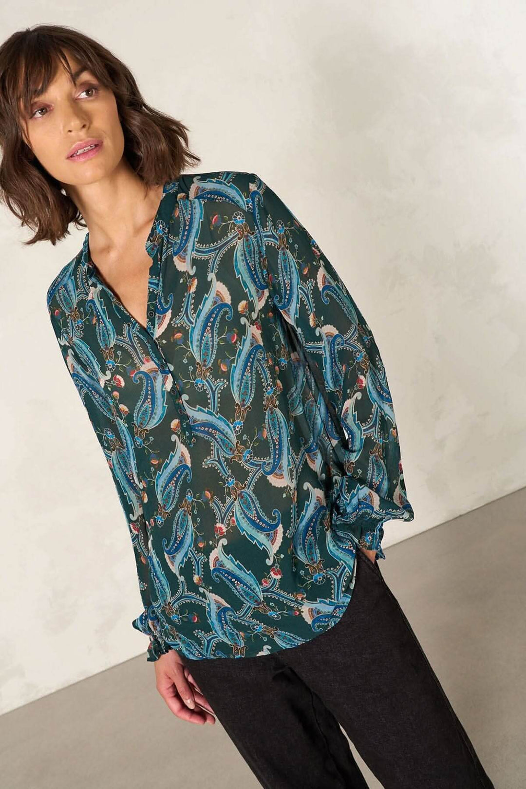 Blouse coupe droite à motifs colorés, manches longues et décolleté en V, portée avec un pantalon noir.