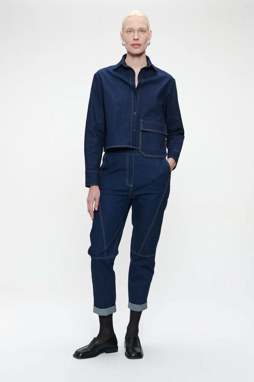 Blouse en denim moderne avec grande poche, surpiqûres contrastantes, coupe droite et col chemise, portée par modèle en studio.