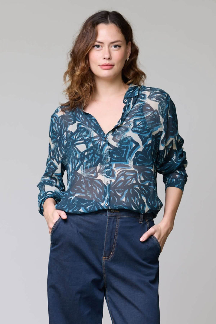 Blouse fluide à imprimé abstrait portée par une femme, tissu léger et élégant, manches longues et col ouvert.