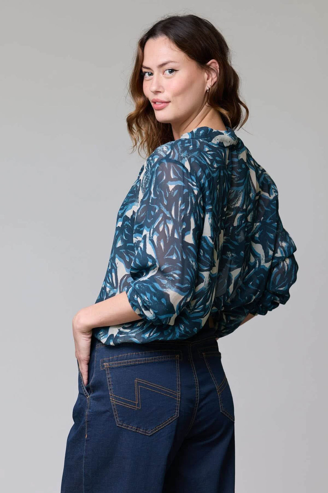 Femme portant une blouse fluide à imprimé abstrait, en tissu léger et élégant, vue de dos avec des manches longues.