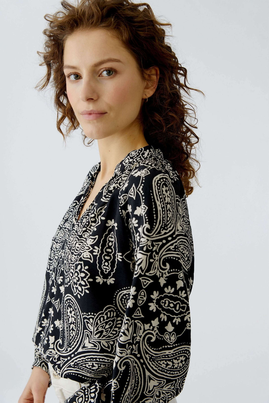 Femme portant une blouse fluide imprimé graphique, coupe droite et encolure ouverte, style bohème chic.