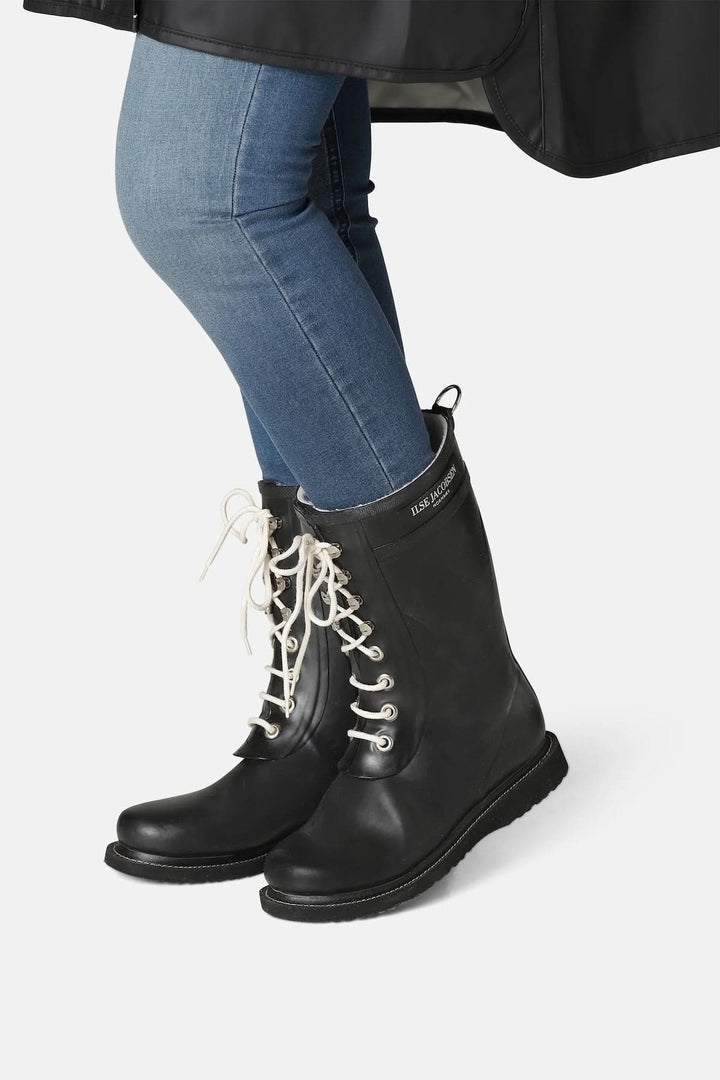 Bottes d’hiver imperméables à lacets en caoutchouc noir avec semelle antidérapante et laçage avant, portées avec un jean