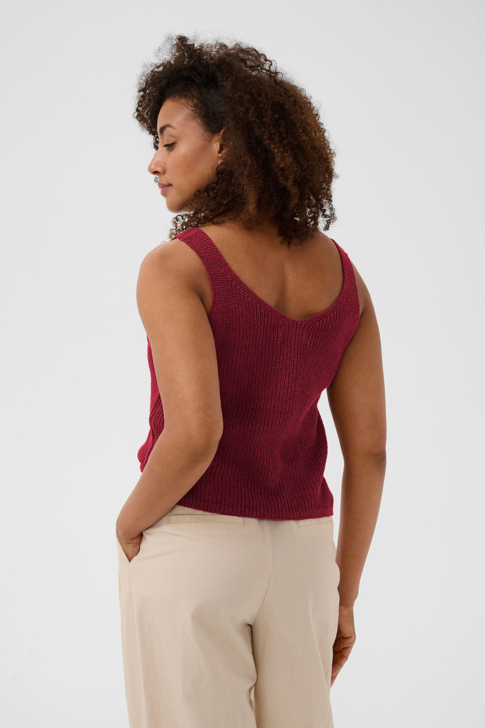 Femme portant une Camisole Rebecca tricotée col v sans manches rouge, maille texturée respirante pour un style estival décontracté.