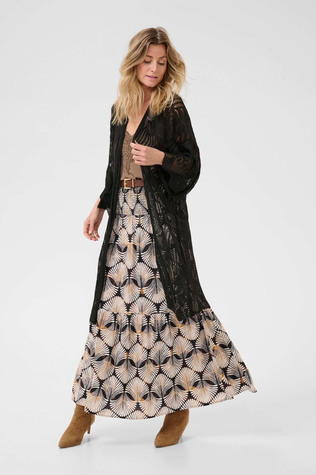 Femme portant un cardigan long en tricot ajouré noir avec une jupe imprimée et des bottines en daim.