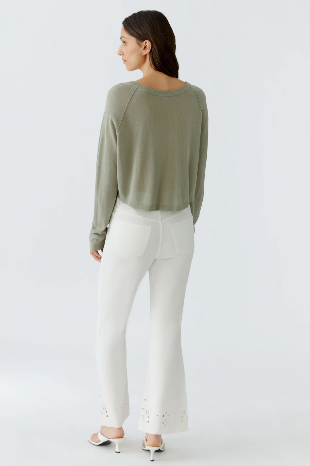 Femme portant un cardigan texturé boutonné élégant et féminin, vu de dos, avec un pantalon blanc, soulignant une allure décontractée.