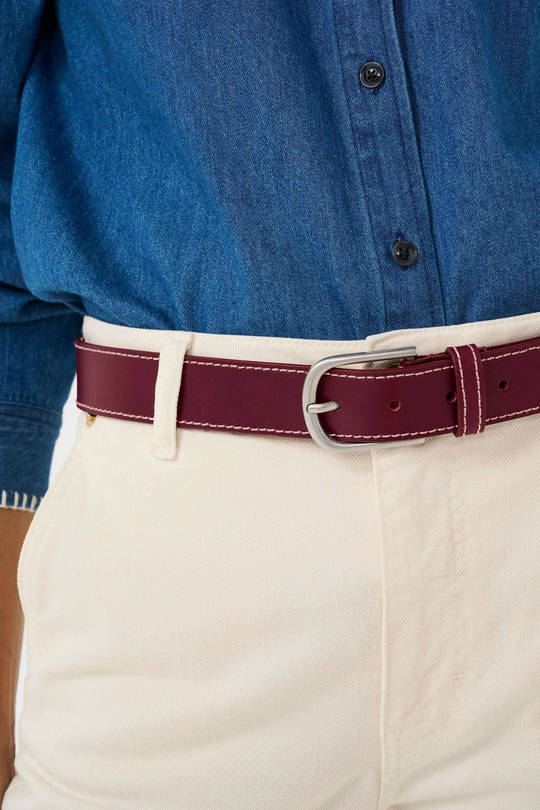 Ceinture Seyra en cuir véritable bordeaux avec surpiqûres contrastantes et boucle métallique classique, portée avec une chemise en jean et un pantalon beige.