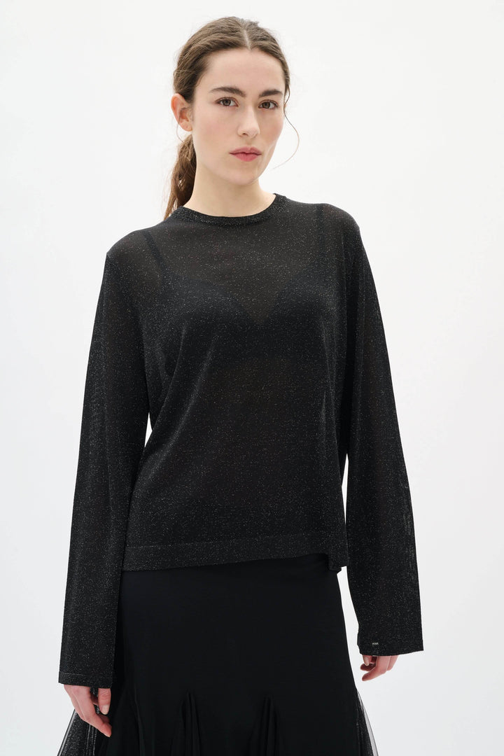 Chandail Thani à effet scintillant noir avec manches longues, matière légère et transparente pour un look élégant et moderne.