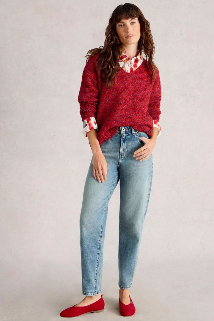 Femme portant un chandail col en V en maille chinée rouge avec chemise à motif et jeans décontractés, look confortable et moderne.