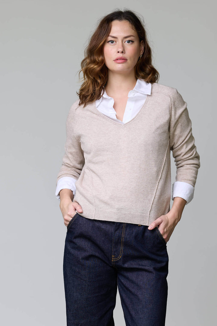 Femme portant un chandail col en V classique beige sur une chemise blanche, combinant élégance et confort.
