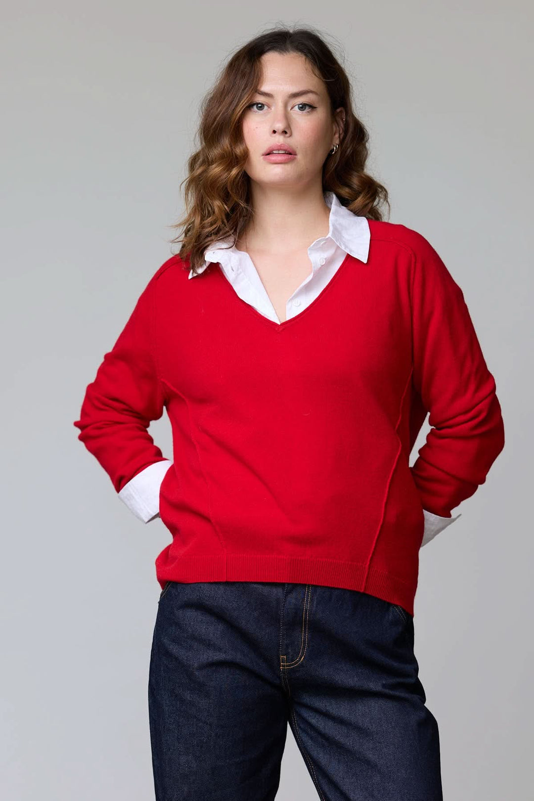 Femme portant un chandail col en V classique rouge avec chemise blanche en dessous, style élégant et polyvalent.
