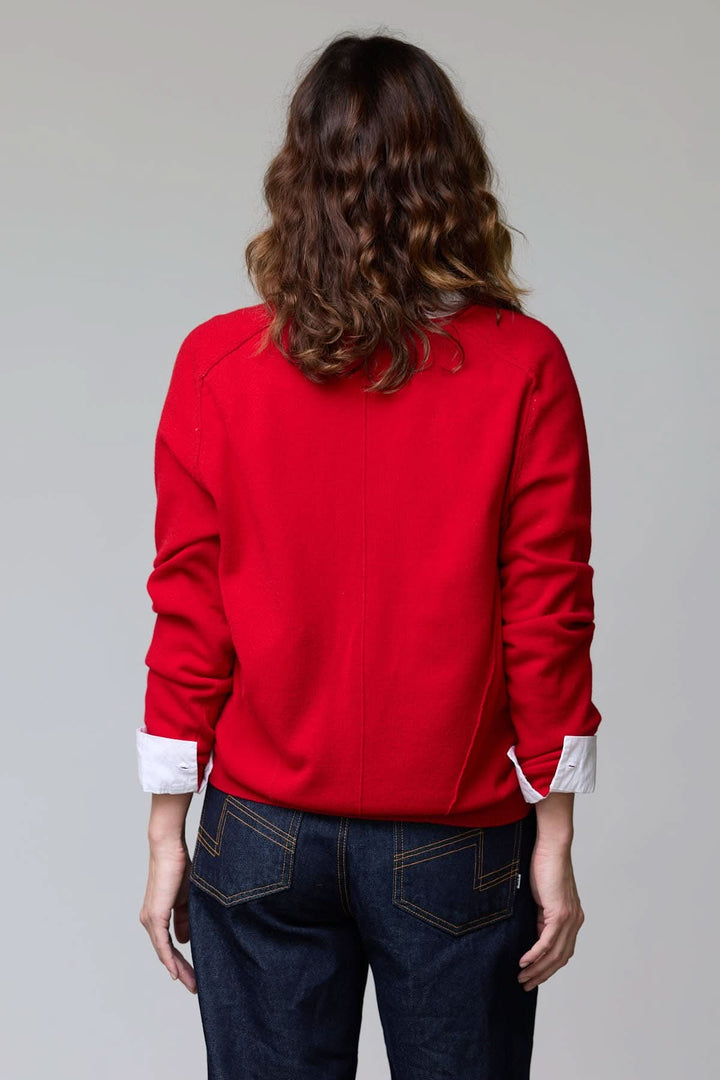 Dos de femme portant un chandail col en V classique rouge, coupe droite avec finitions côtelées, sur une chemise blanche et un jean.
