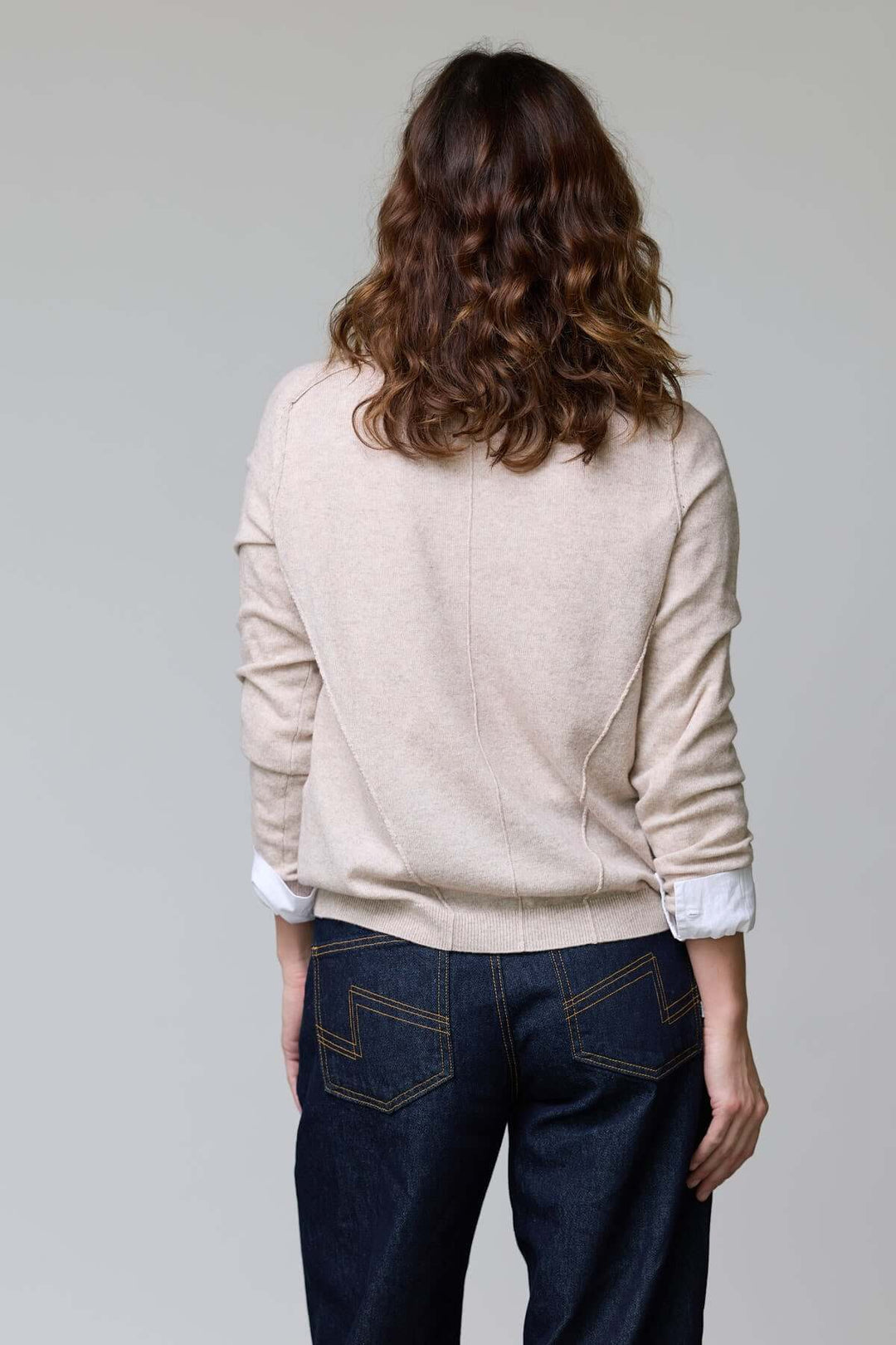 Chandail col en V classique en maille beige porté avec un jean, vue de dos. Le chandail est intemporel et élégant pour un look raffiné.