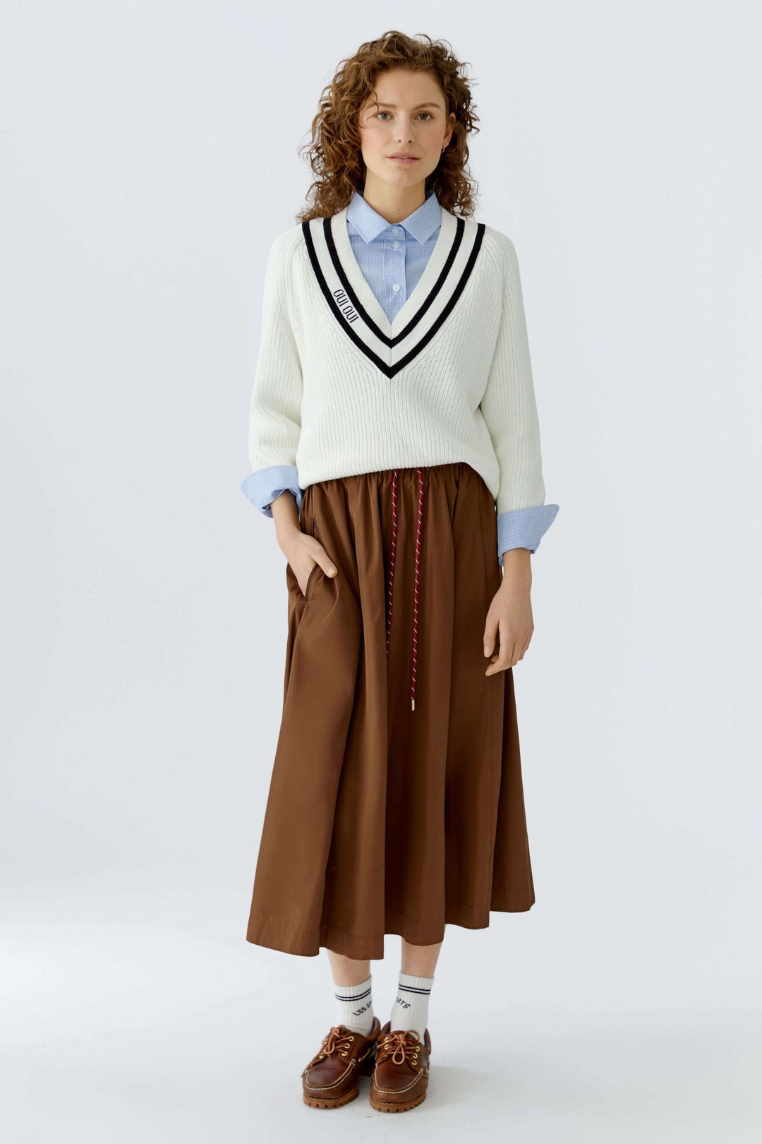 Femme portant un chandail en maille encolure en V avec chemise et jupe, ajoutant une touche moderne à une tenue classique.