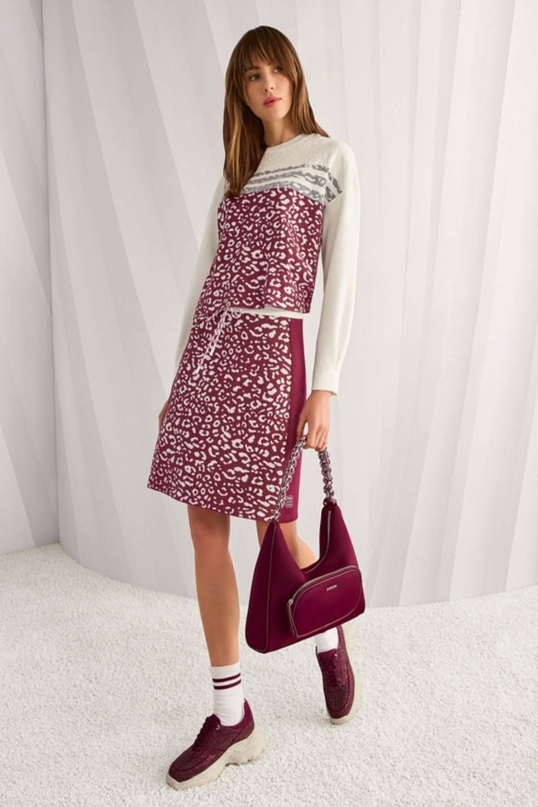 Femme portant un chandail en tricot manches longues imprimé graphique et empiècements contrastants, avec jupe et sac assortis.