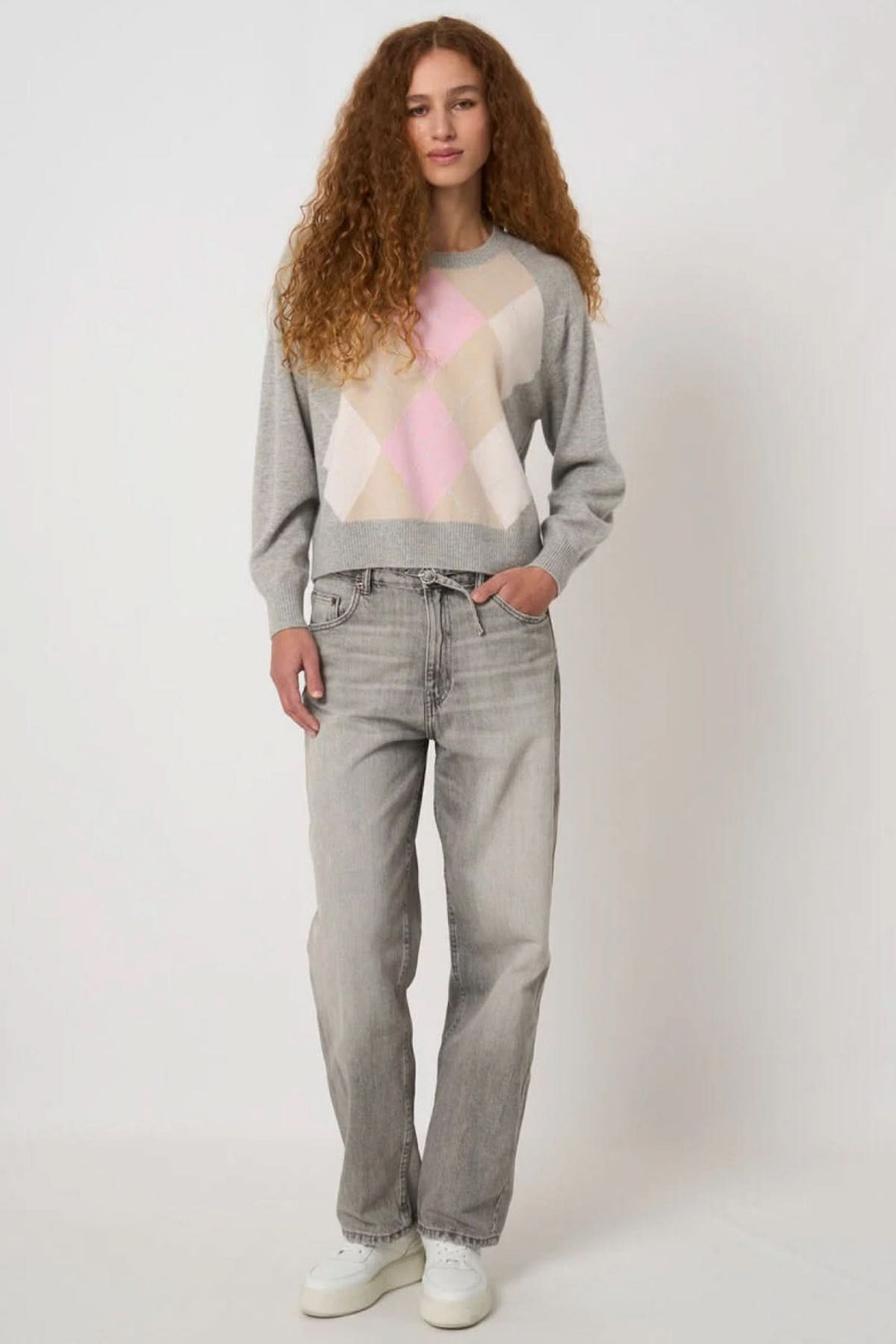 Femme portant un chandail en tricot avec motif géométrique rose, coupe droite, style décontracté et intemporel.