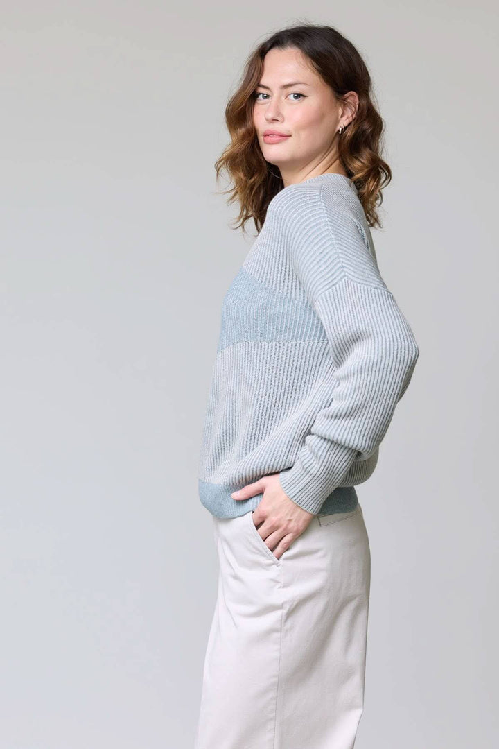 Femme portant un chandail en tricot côtelé gris avec manches longues et coupe décontractée, idéal pour un look quotidien moderne.