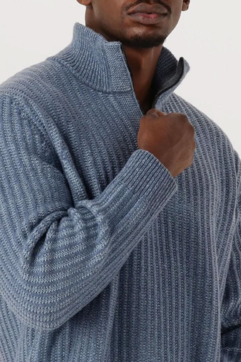 Homme portant un chandail en tricot à demi-glissière côtelé bleu avec un col montant zippé et des détails côtelés, style classique et moderne.