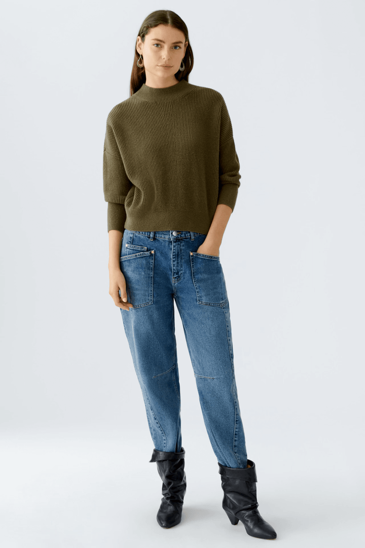 Femme portant un chandail maille fine avec col montant, manches longues, et un jean décontracté, affichant un style chic et moderne.