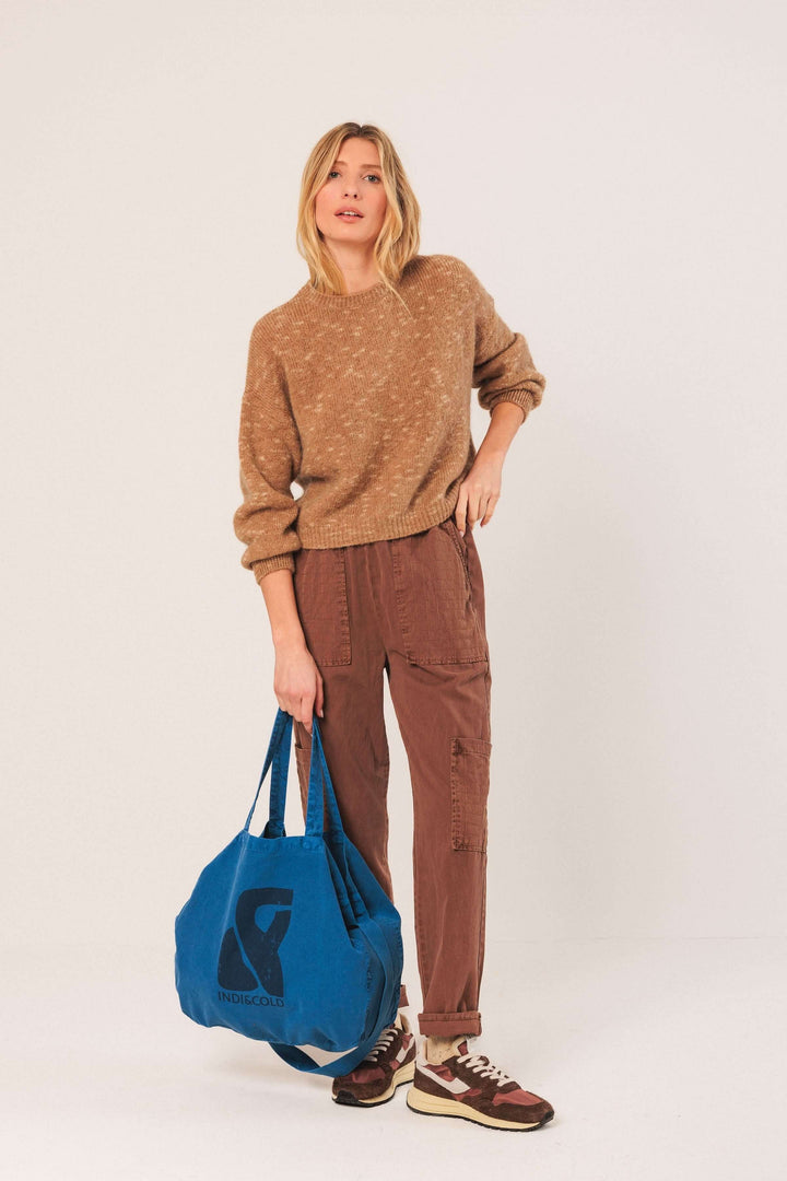 Femme portant un chandail maille texturée marron avec pantalon décontracté et sac bleu, style automnal moderne.