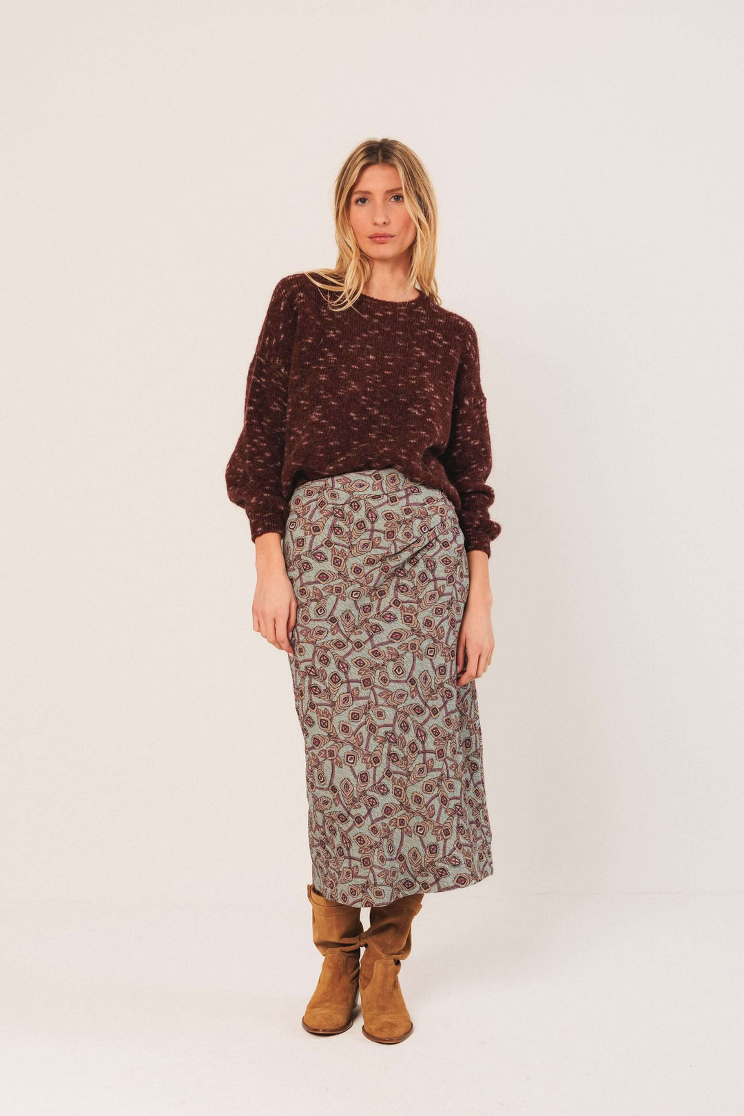 Femme portant un chandail maille texturée avec jupe imprimée et bottes, style décontracté, mode hivernale chic et tendance.