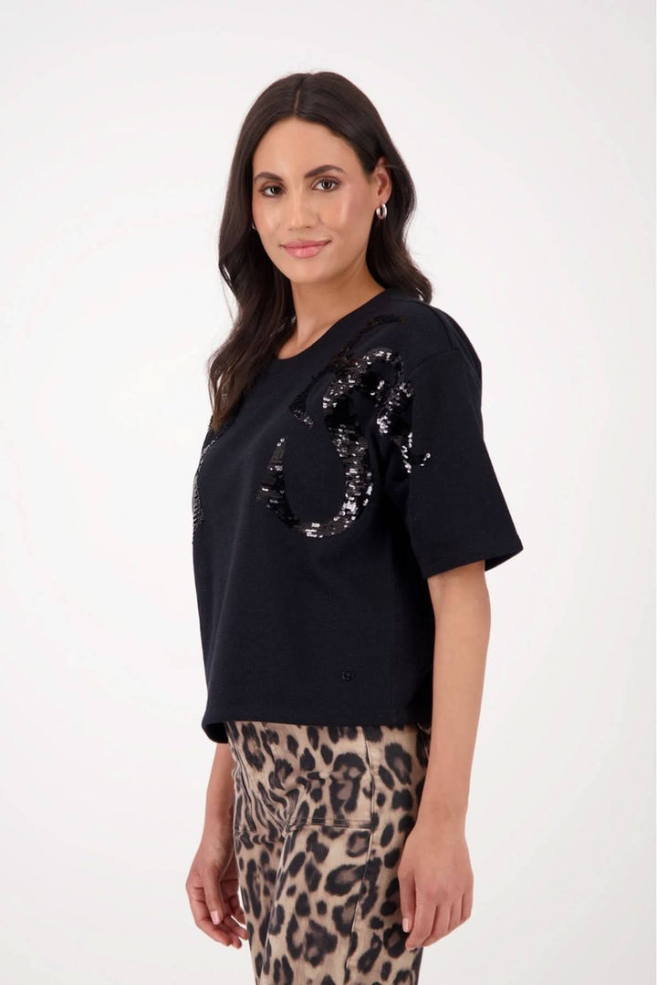Chandail à manches courtes noir avec appliqués de paillettes ton sur ton, coupe droite et col rond, porté avec jupe imprimée léopard.