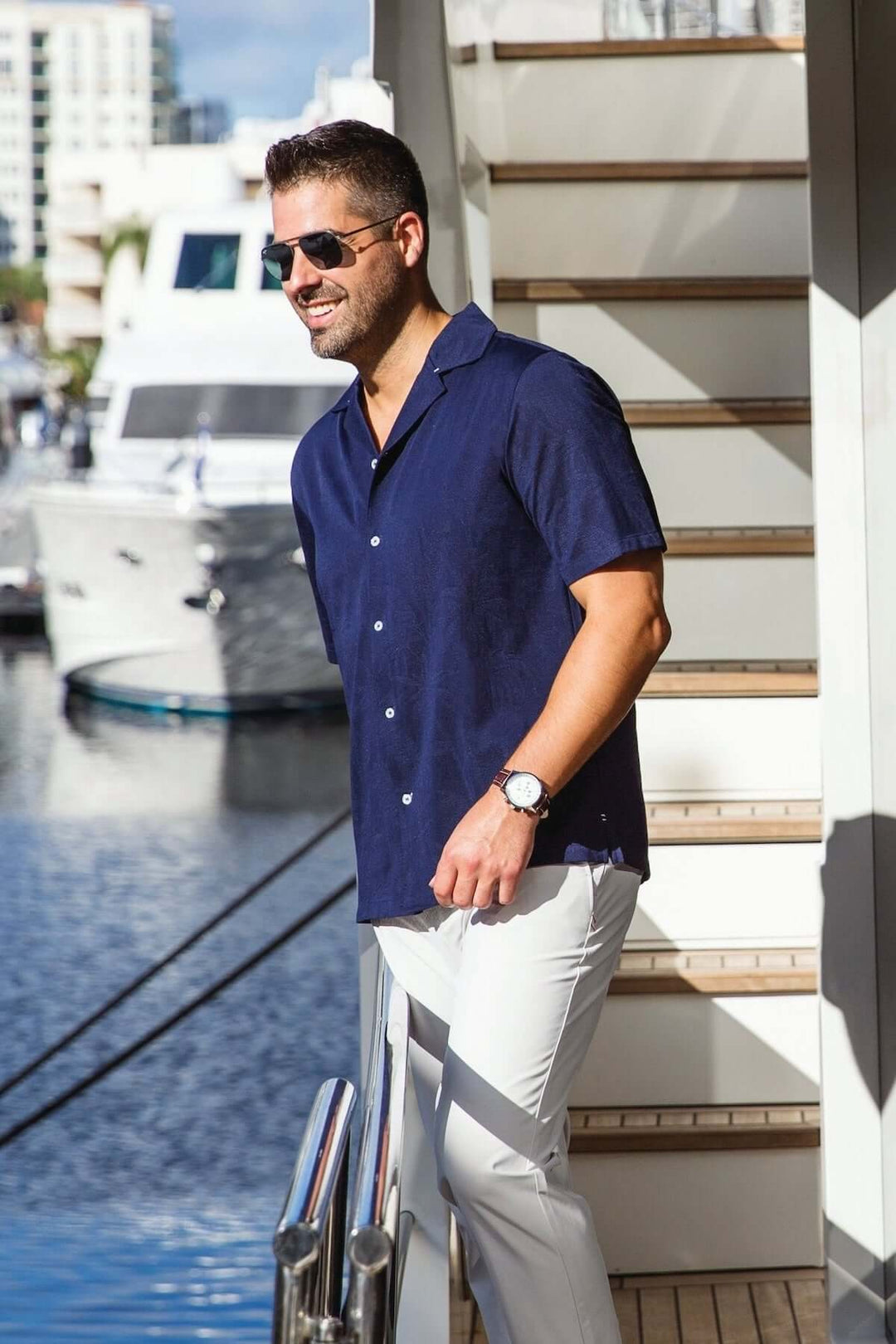 Homme portant une chemise à manches courtes bleu marine, lunettes de soleil, marchant au bord d&