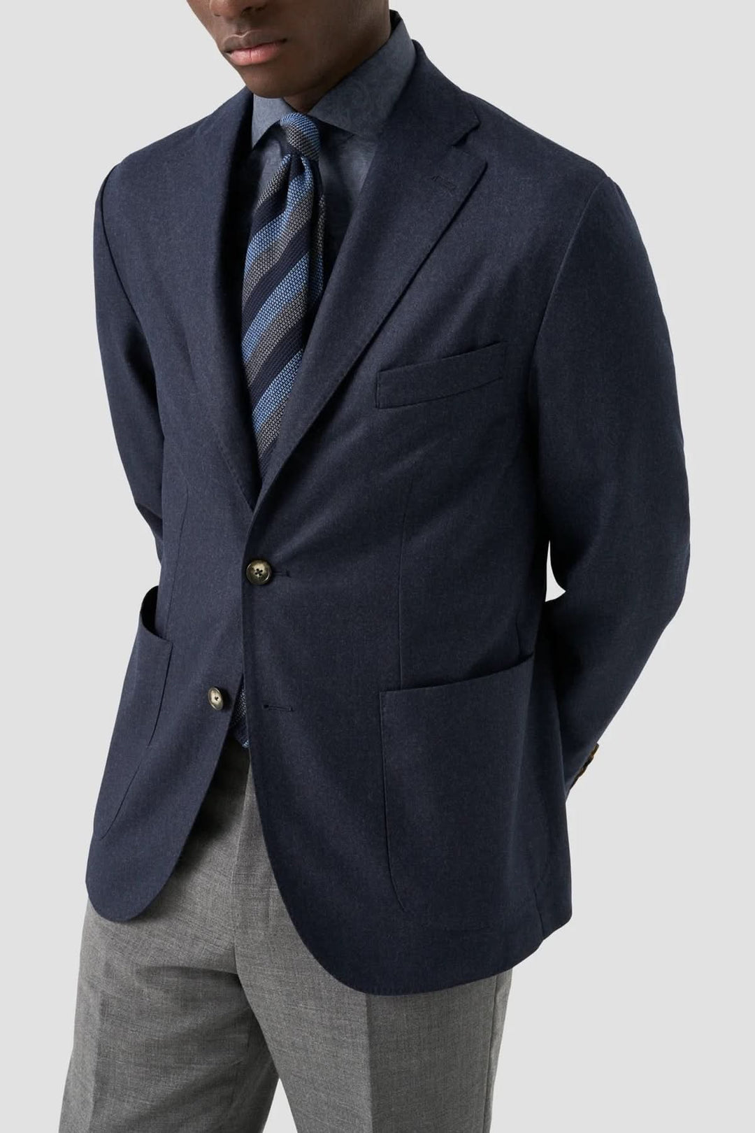 Homme portant une veste bleue élégante avec une cravate rayée et un pantalon gris