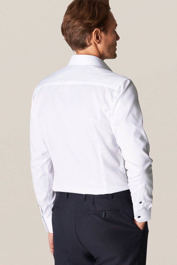 Homme portant une chemise blanche élégante avec boutons contrastés, vue de dos, style business.