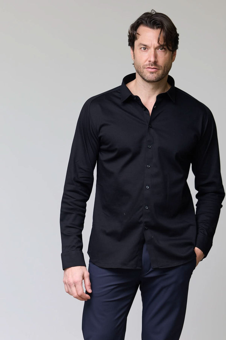 Homme portant une chemise en jersey extensible noire à manches longues et col classique, coupe ajustée moderne.