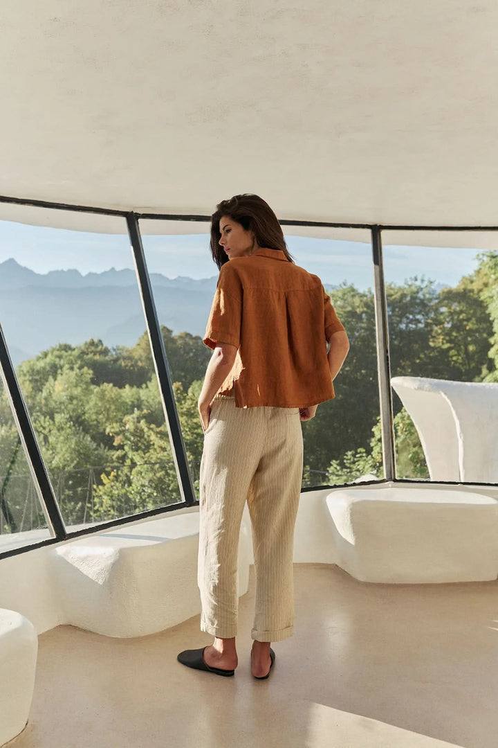 Femme portant une chemise en lin à coupe décontractée devant une fenêtre avec vue sur la montagne, décris moi le produit en français.