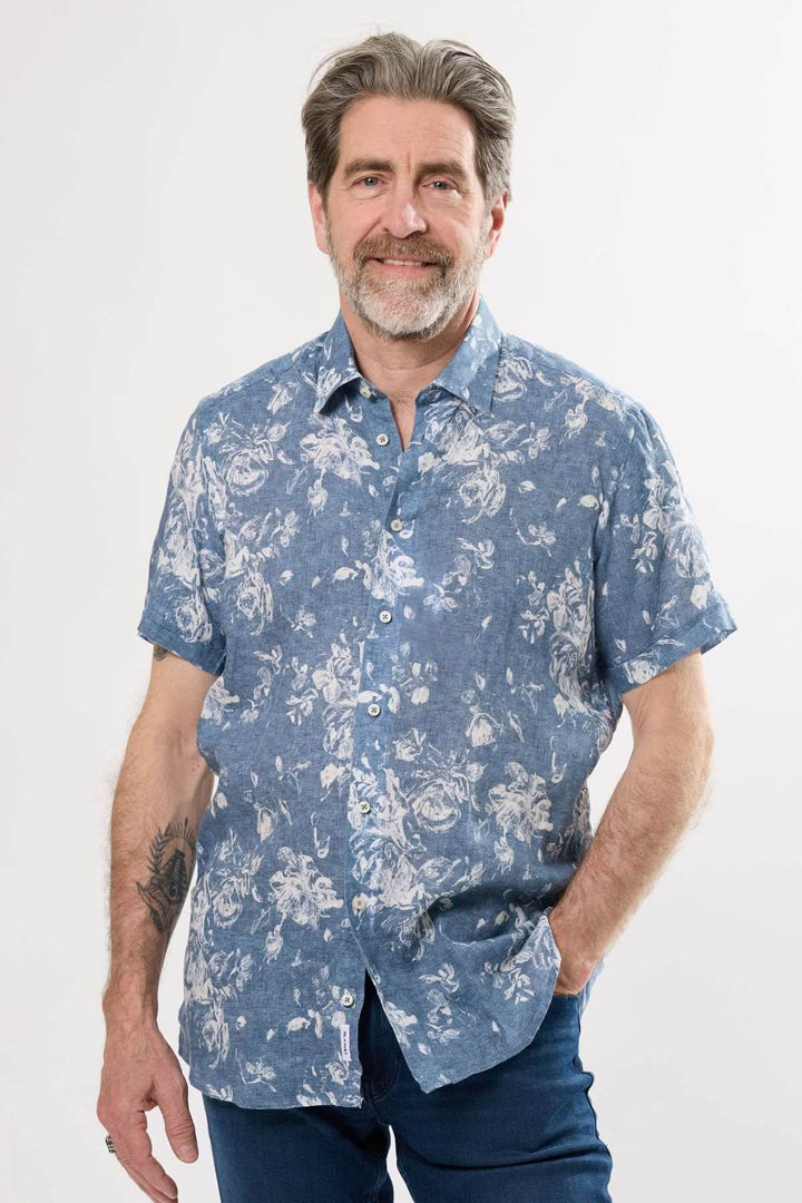 Homme souriant portant une chemise à manches courtes à motif floral sur fond chambray, idéal pour l&