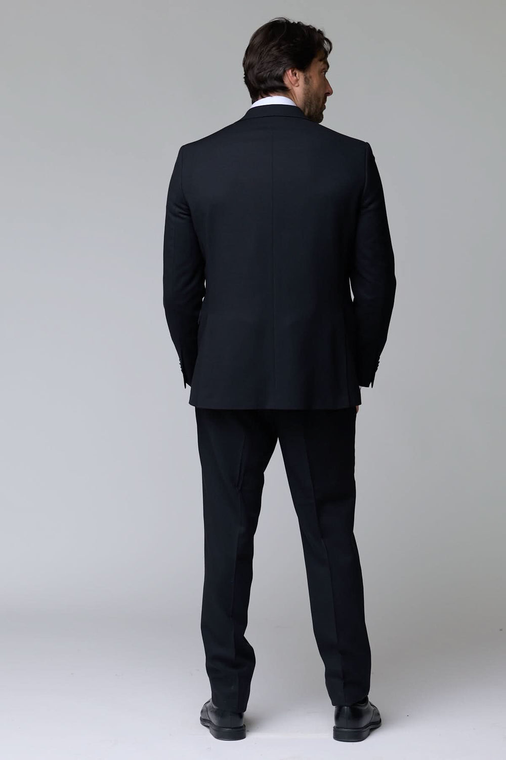 Homme portant un complet classique deux pièces noir, vue de dos, élégant pour le bureau et occasions formelles.