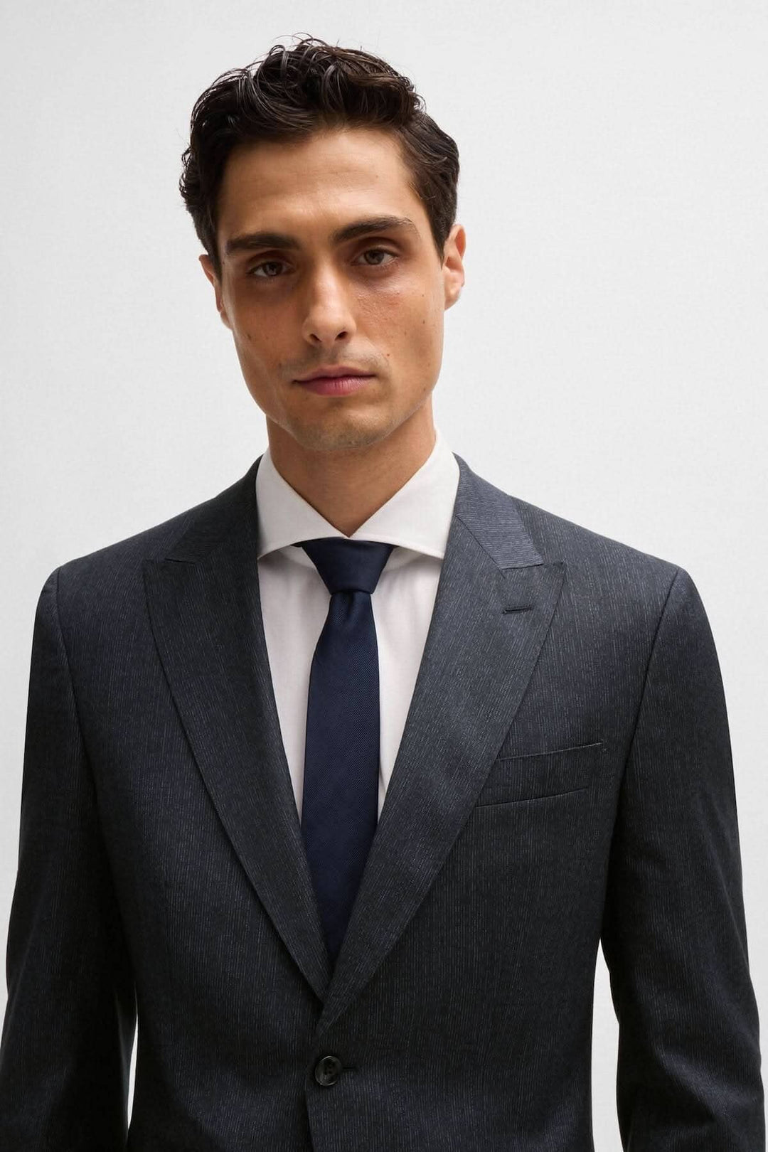 Homme en complet slim moderne avec veste aux épaules structurées, portant une chemise blanche et une cravate bleue.