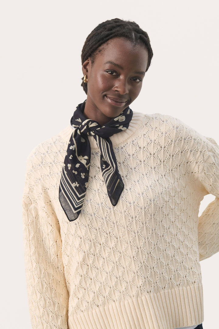 Foulard Phi élégant en coton, porté autour du cou avec un pull crème, ajoutant une touche de fraîcheur.
