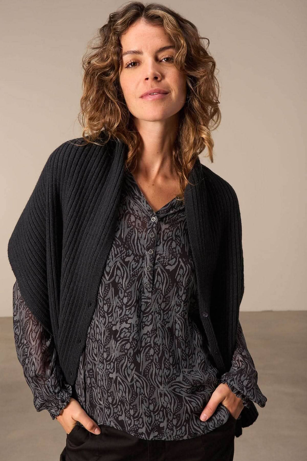 Foulard cape en tricot noir porté avec un haut à motifs, offrant élégance et confort.