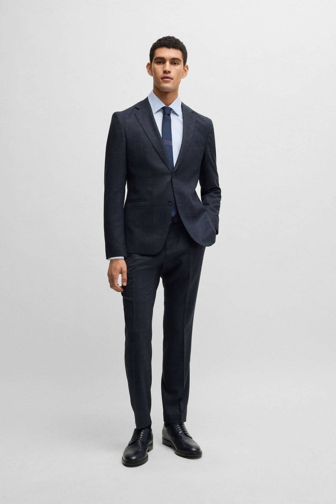 Homme en costume deux pièces BOSS moderne, noir, avec cravate, pose sobre sur fond neutre.