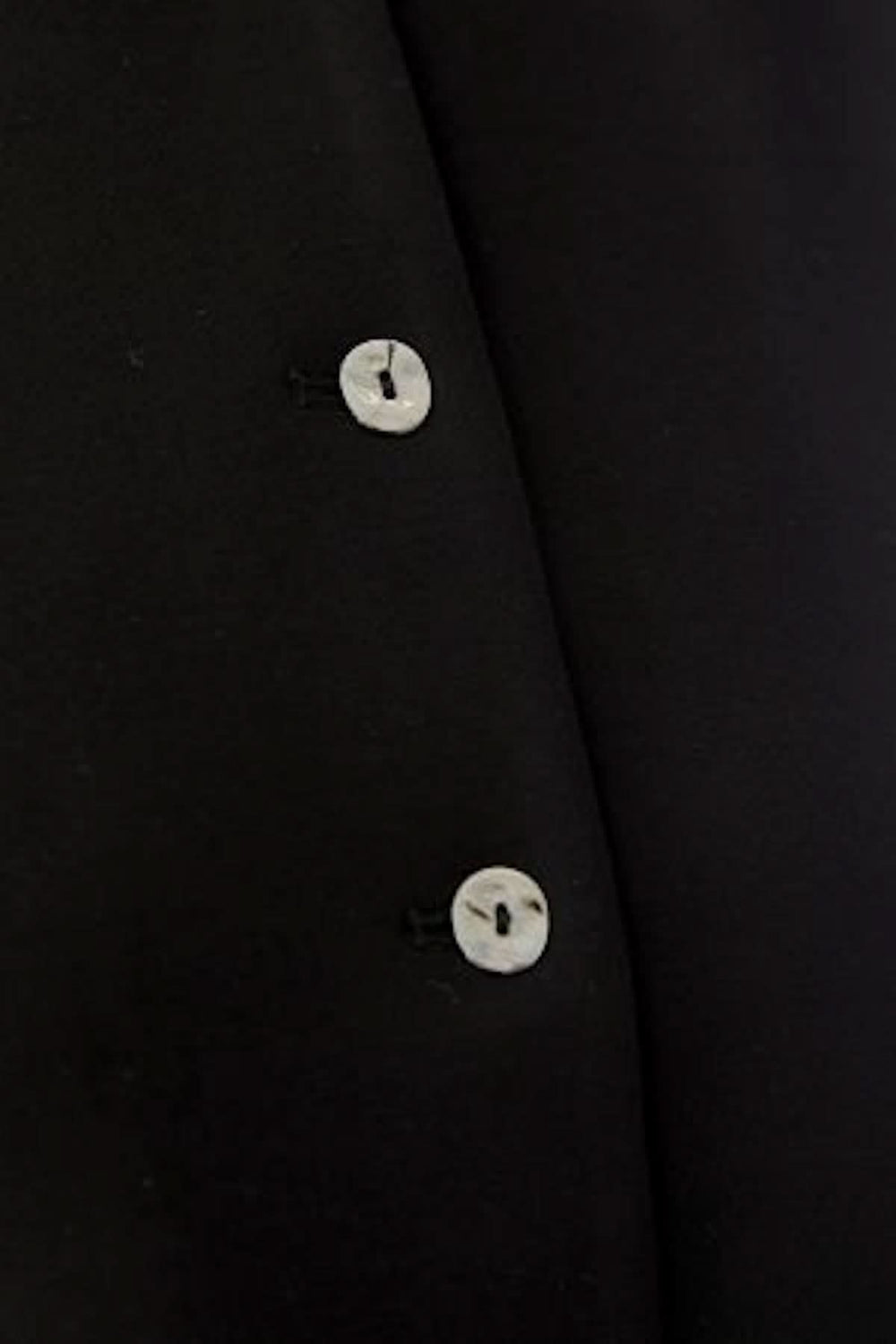 Détail bouton du haut sans manches boutonné, design sobre et élégant en noir, parfait pour une tenue moderne et minimaliste.