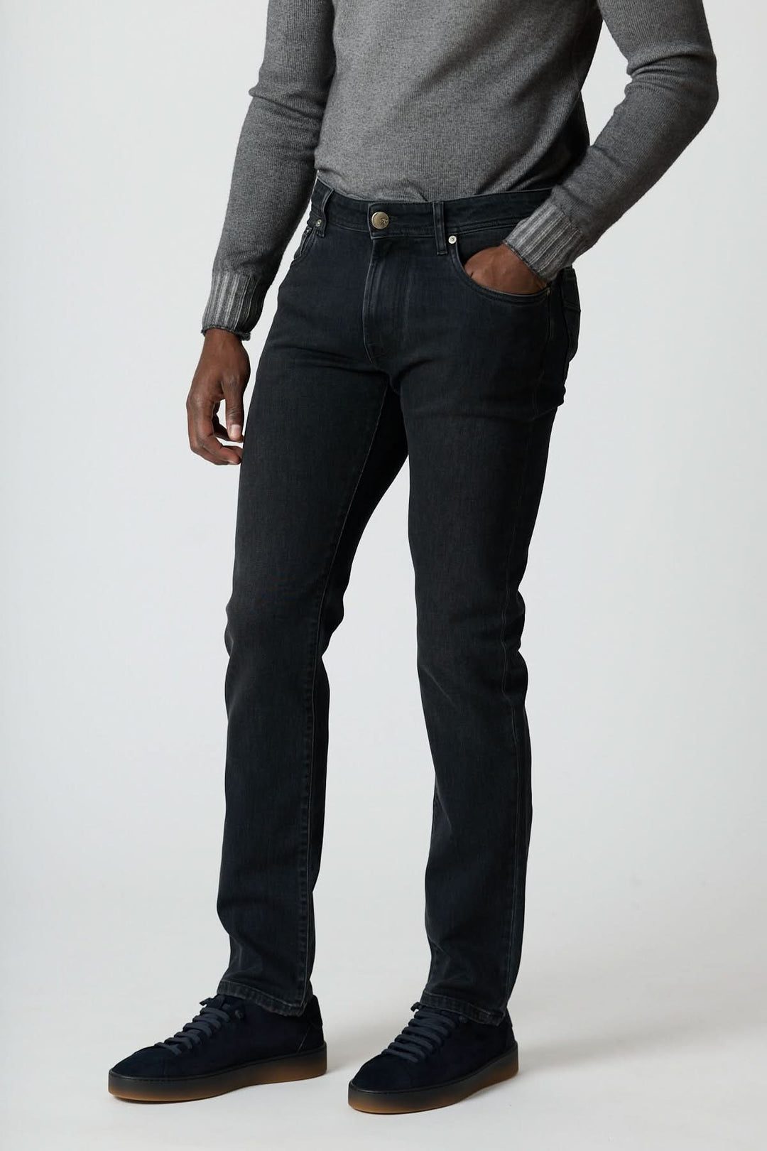 Jean 5 poches en denim stretch gris foncé, coupe ajustée, tenue impeccable, porté avec pull gris et sneakers propre.