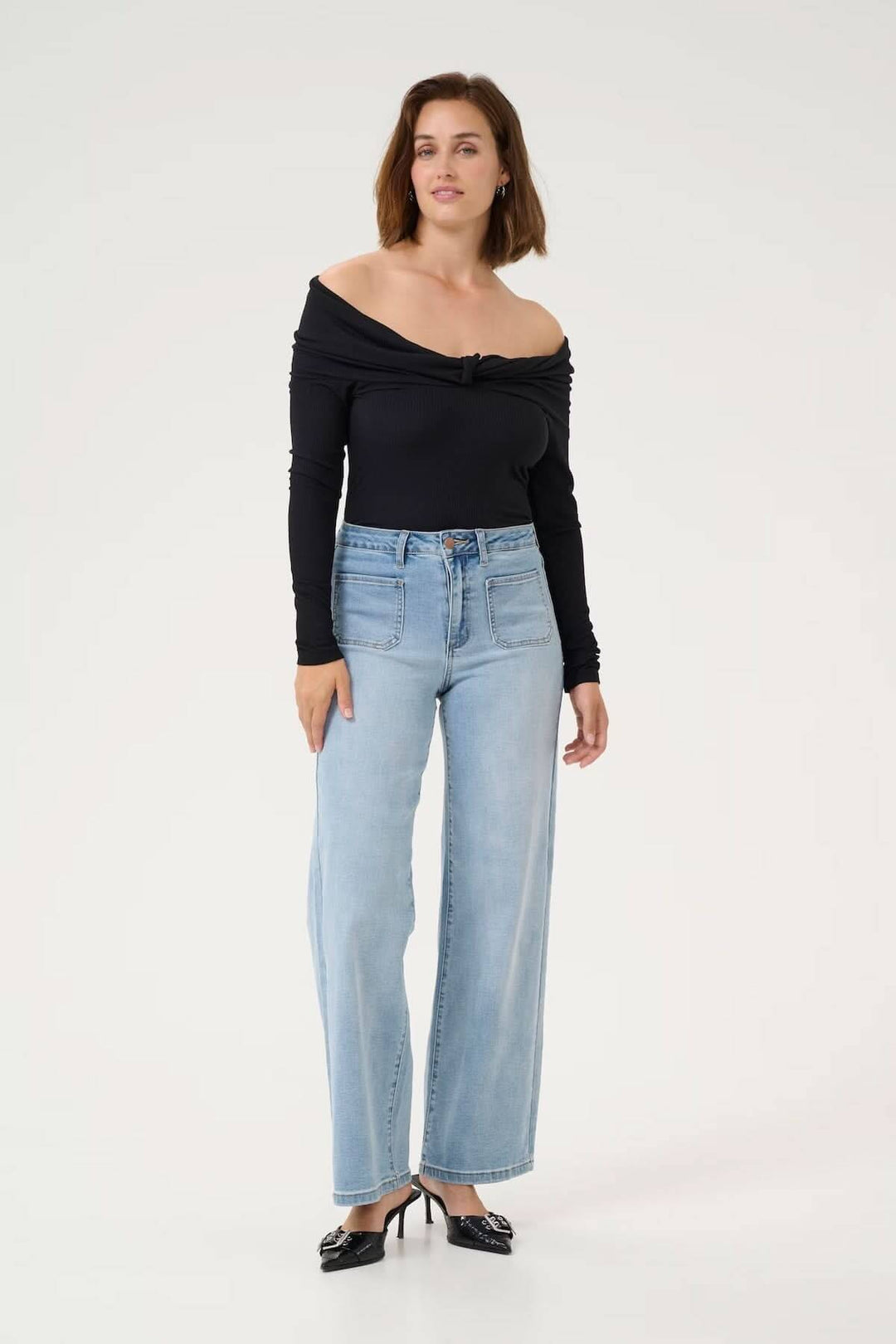 Femme portant un jean à coupe large, taille haute, avec un top noir en décolleté, style moderne et décontracté.