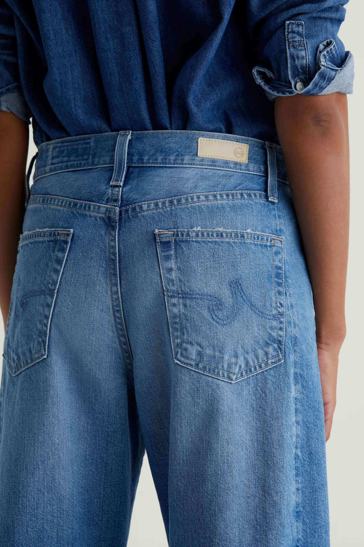 Jean droit à jambe large en denim bleu avec taille haute, vu de dos, mettant en valeur les détails des poches et le tissu en coton pur.