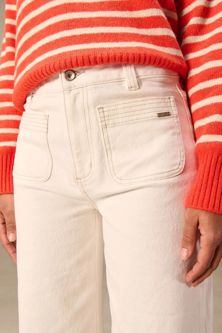 Jean jambe large blanc avec poches appliquées, taille haute et pull rayé rouge, parfait pour un look décontracté et moderne.