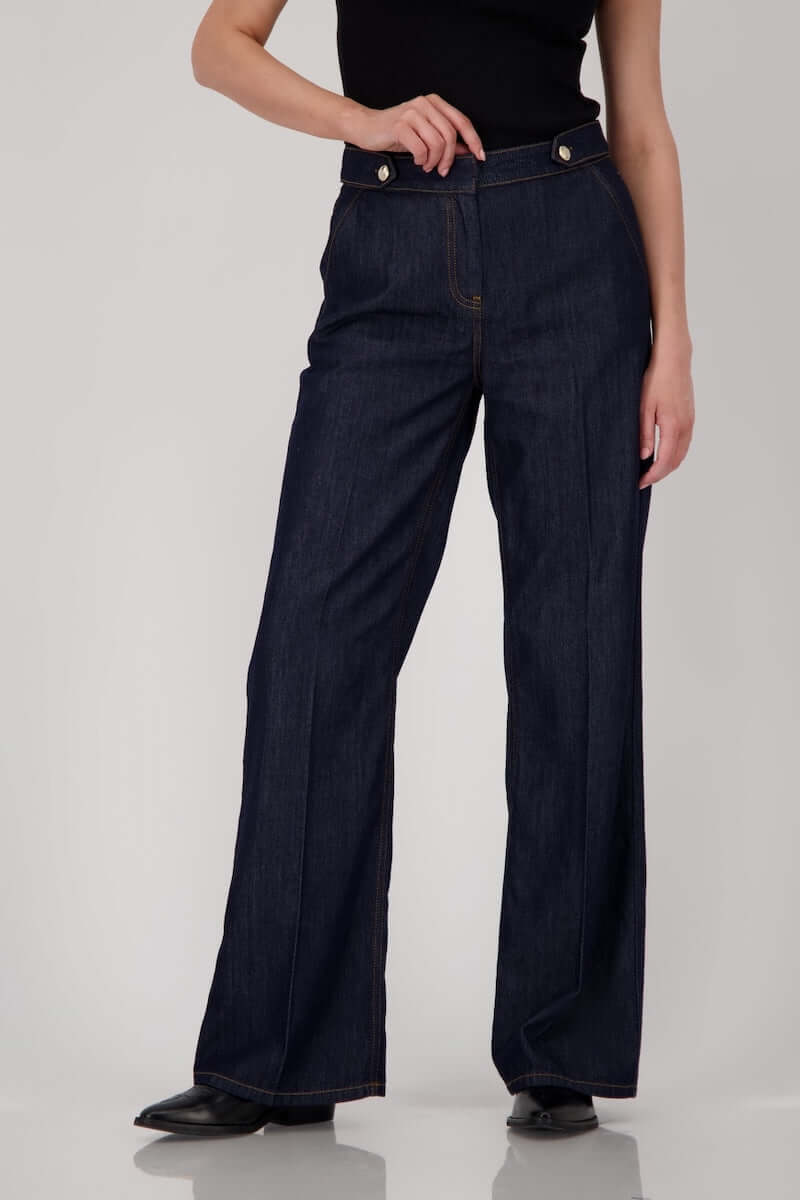 Jean taille haute en denim brut, coupe droite avec boutons métalliques et coutures visibles, longueur chevilles.