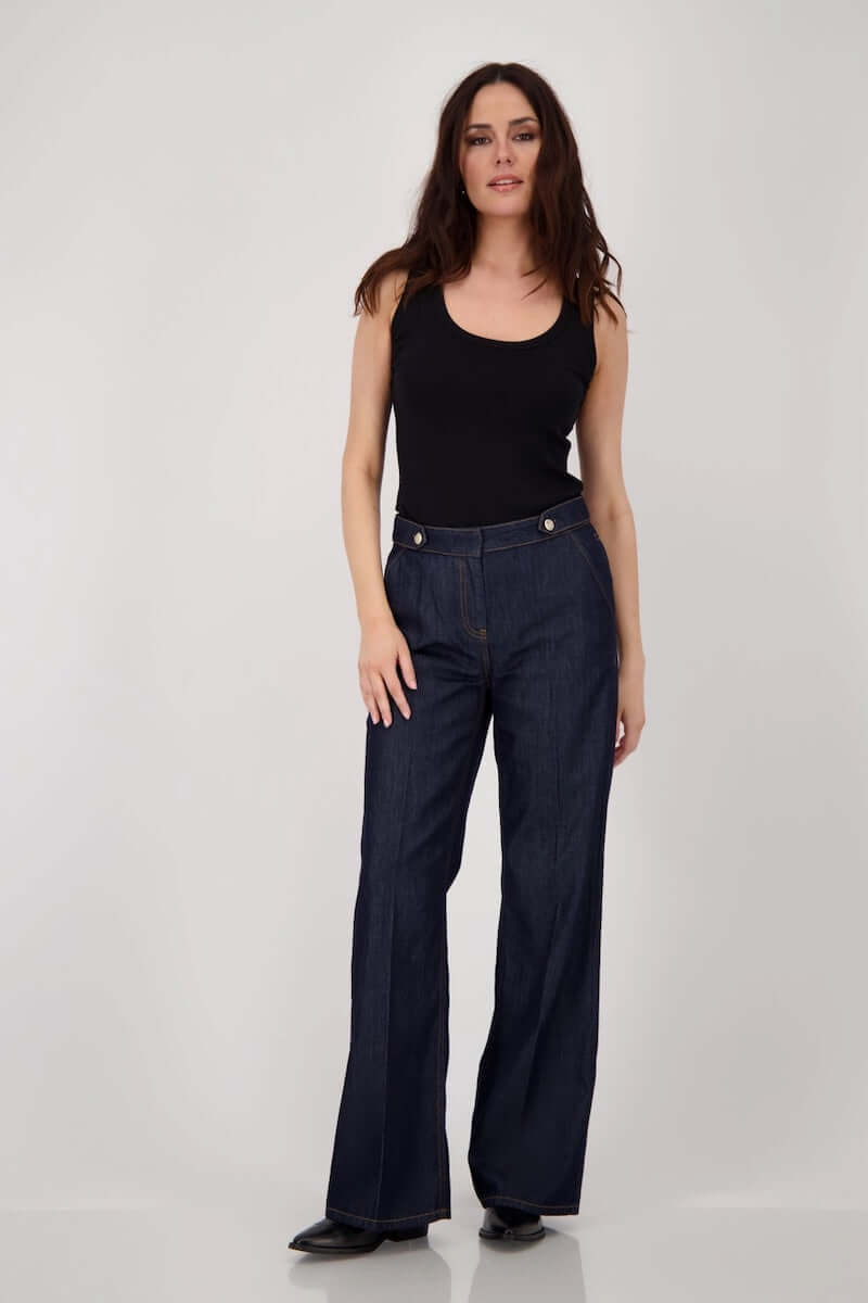 Jean taille haute en denim brut, coupe droite et ample, porté par une femme, avec coutures visibles et boutonnière métallique.