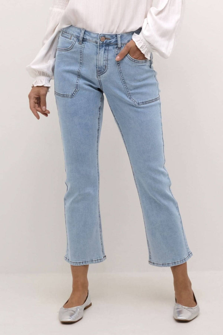 Jeans bleu clair à coupe droite, taille régulière, longueur 7/8, porté avec une blouse légère et des ballerines.