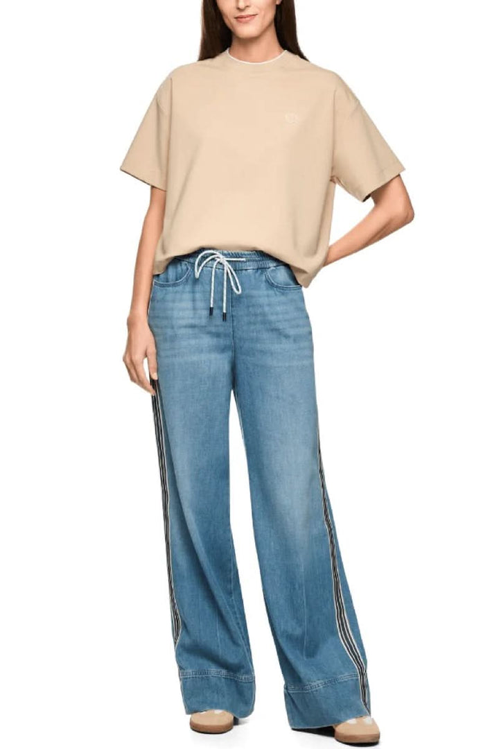 Jeans large à bandes contrastantes avec taille élastique et cordon, style moderne et sportif, porté avec un t-shirt beige décontracté.